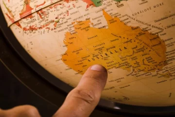 a imagem mostra um dedo apontando para a Austrália, num globo.